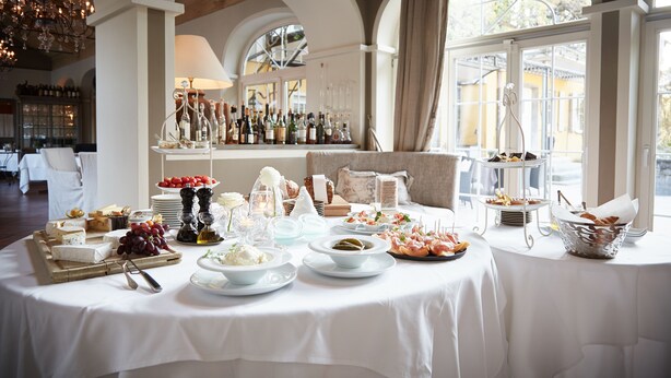 Una mesa de buffet con diversos alimentos y una selección de vinos en una sala con techos abovedados y ventanas grandes.