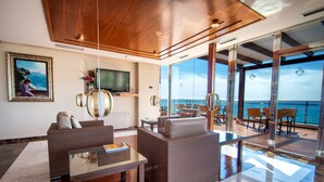 A modern living room with a large TV, comfortable seating, and a view of the sea through large windows. - Hotel Servigroup Montíboli (Villajoyosa)
