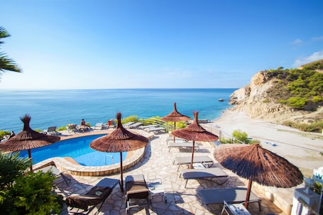 A poolside area with lounge chairs and thatched umbrellas, overlooking a beach and the sea.
