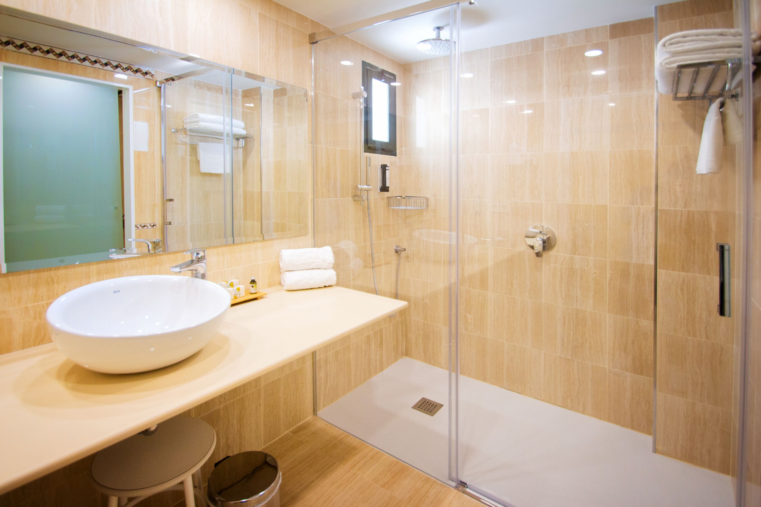Un baño moderno con un lavabo grande de color blanco, cabina de ducha con mampara de cristal y un espejo sobre el lavabo.