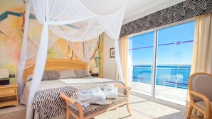 A hotel room with a bed, a bench with towels, a chair, a nightstand, and a large window with a view of the sea. - Hotel Servigroup Montíboli (Villajoyosa)