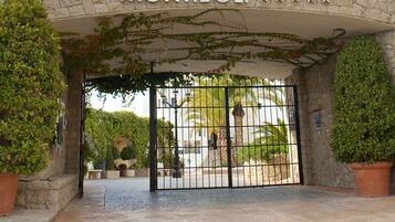 De ingang van Hotel Servigroup Montiboli, met een stenen boog, vlaggen en een hekwerk.