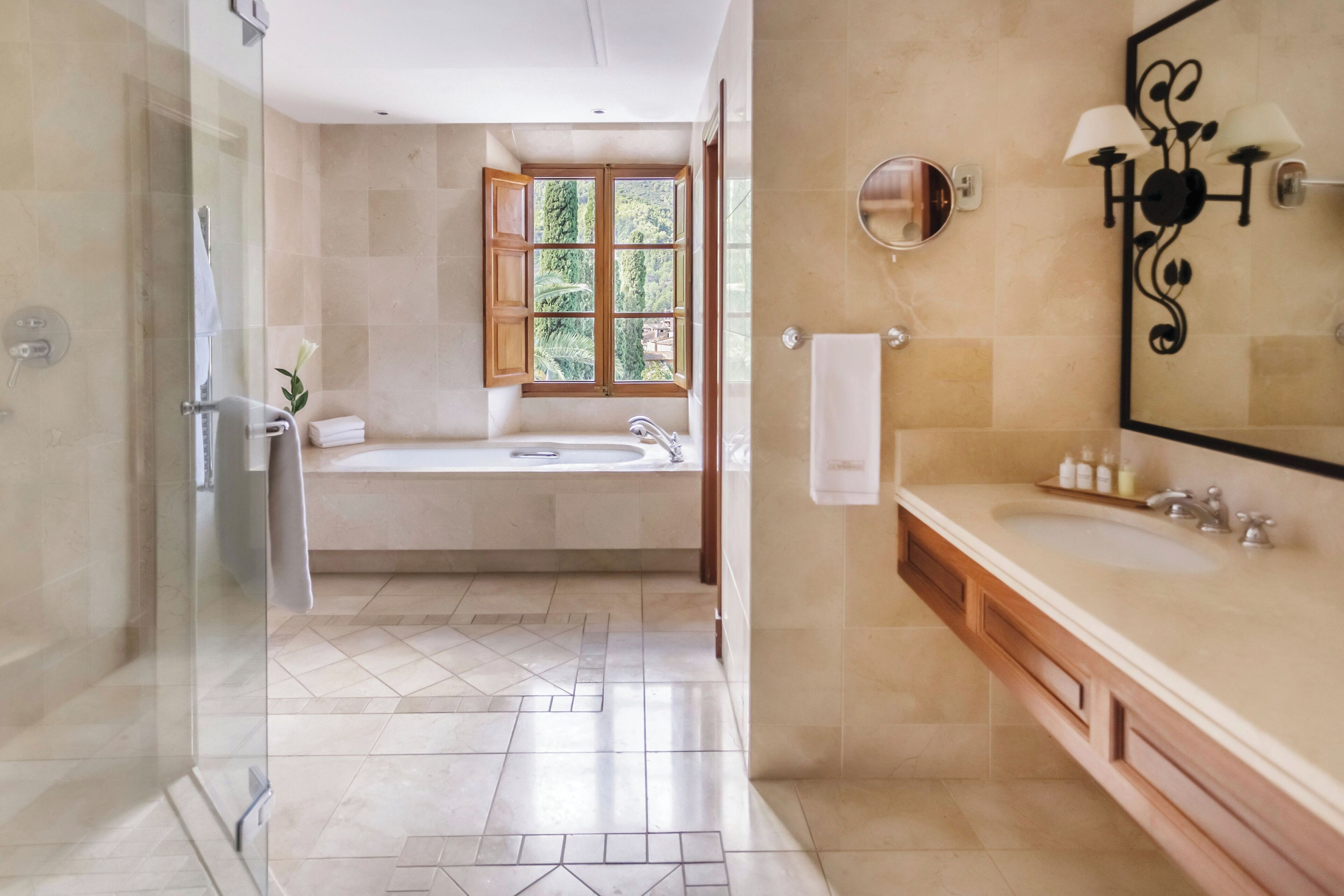 Un baño moderno con cabina de ducha de vidrio, bañera independiente, tocador con un espejo grande y ventana que proporciona luz natural.