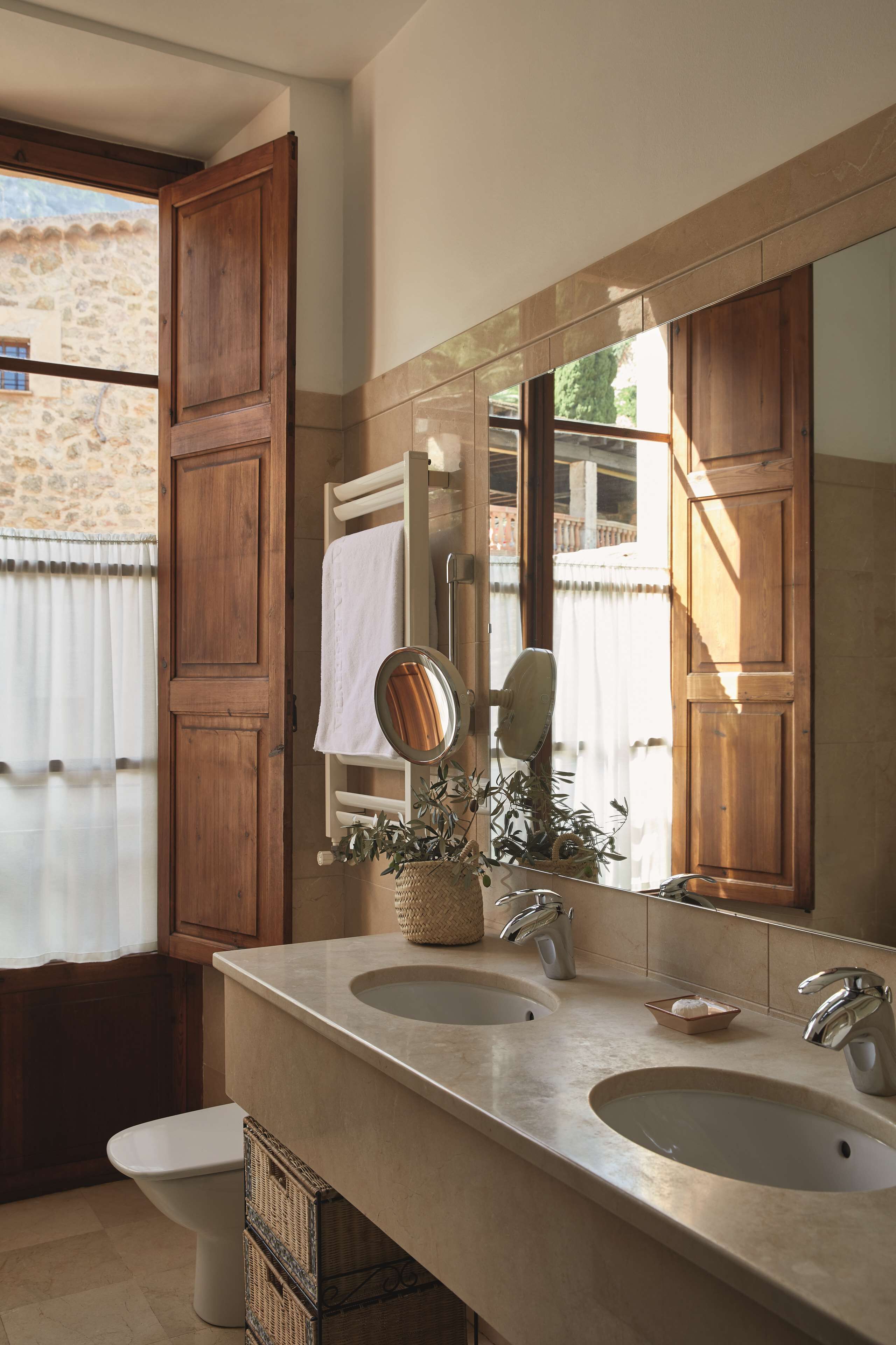 A bathroom with two sinks, a large mirror, and a window with wooden shutters.