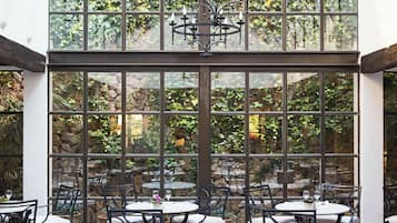 Une véranda avec des tables et des chaises, de grandes fenêtres et un lustre.