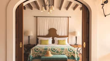 Un dormitorio con cabecera de madera, dos mesitas de noche con lámparas, una cama con colcha estampada, un banco y un arco de entrada.