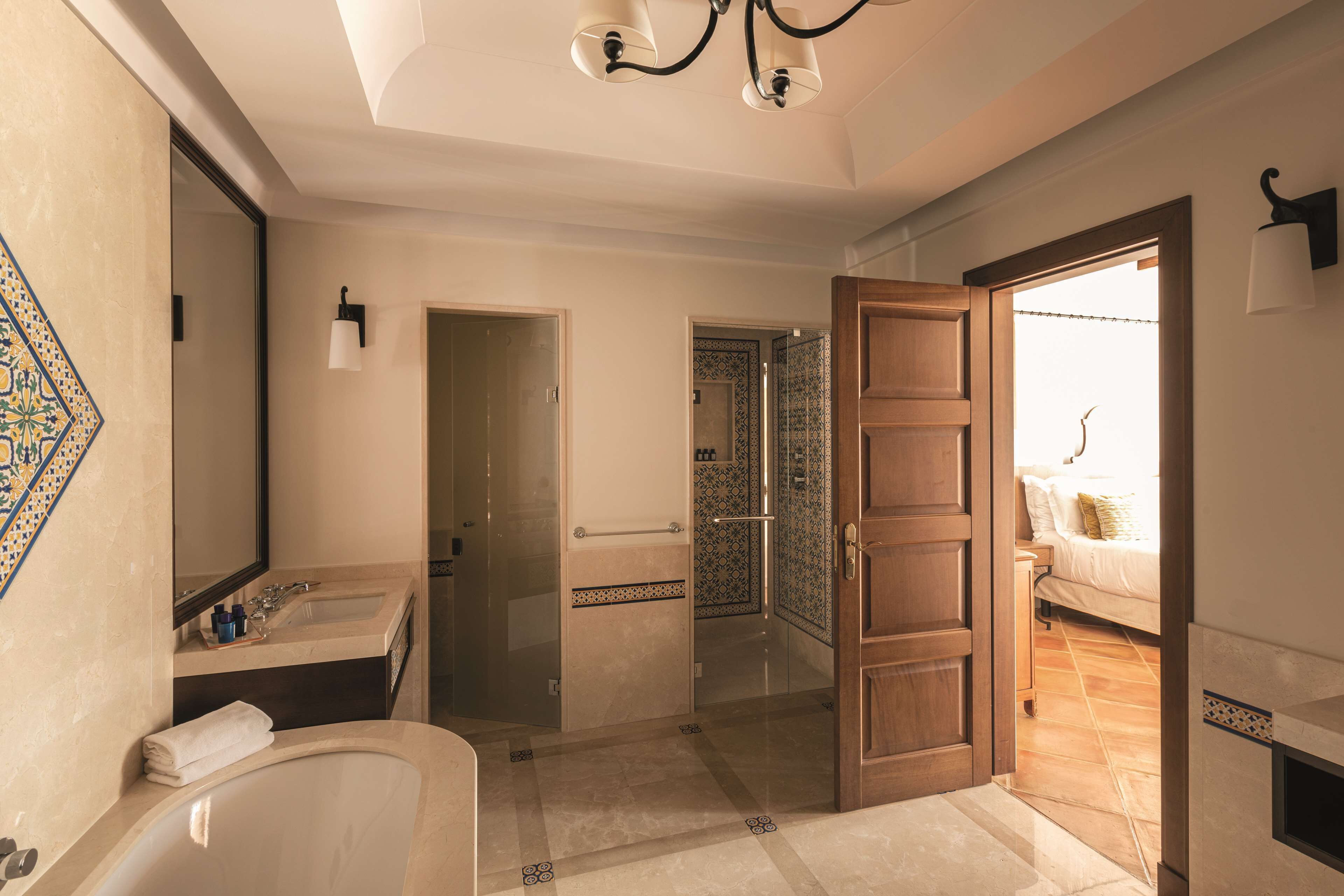 A bathroom with a bathtub, a sink, and a mirror. There is a door leading to a bedroom.