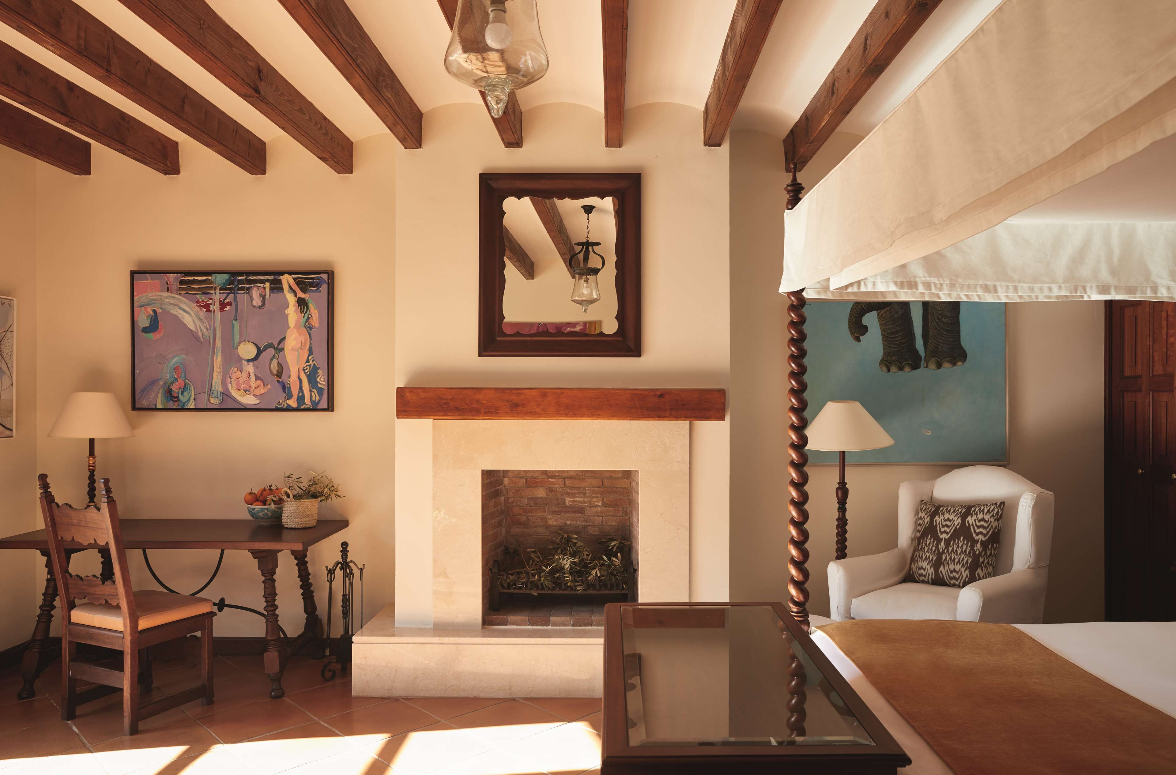 A room with a fireplace, wooden beams, a dining table with chairs, and a bed.