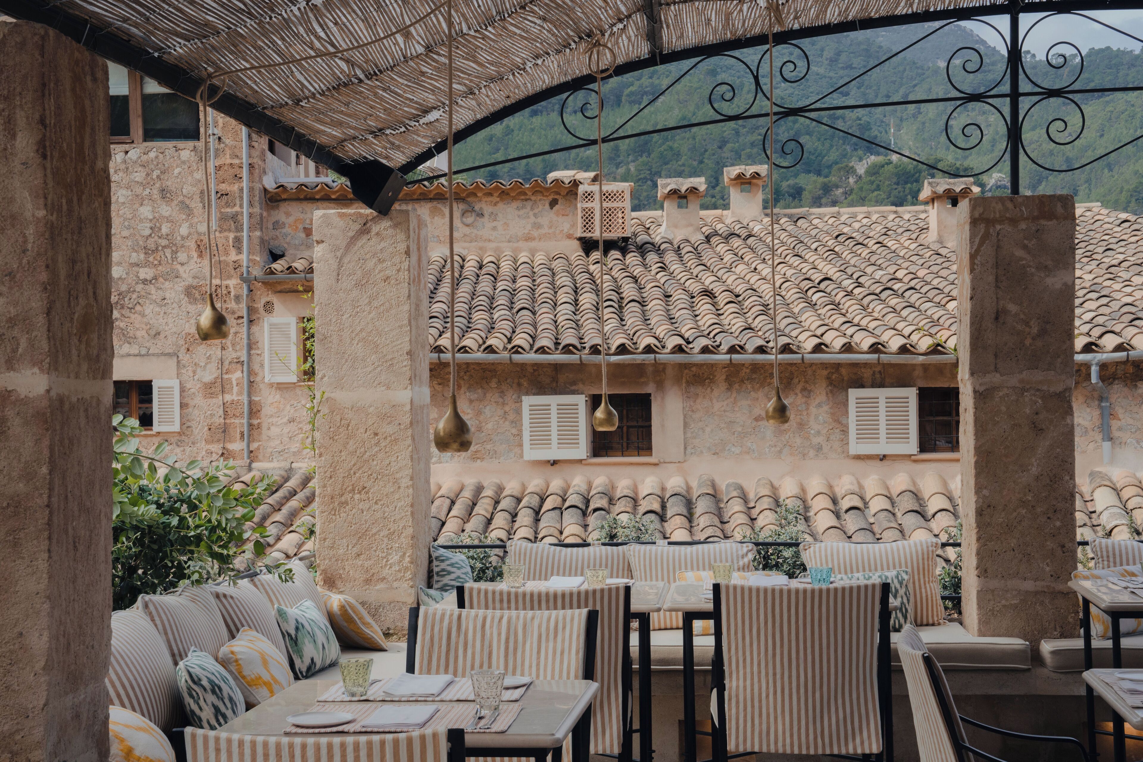 Une terrasse extérieure avec des tables et des chaises, des murs en pierre et un toit recouvert de tuiles.