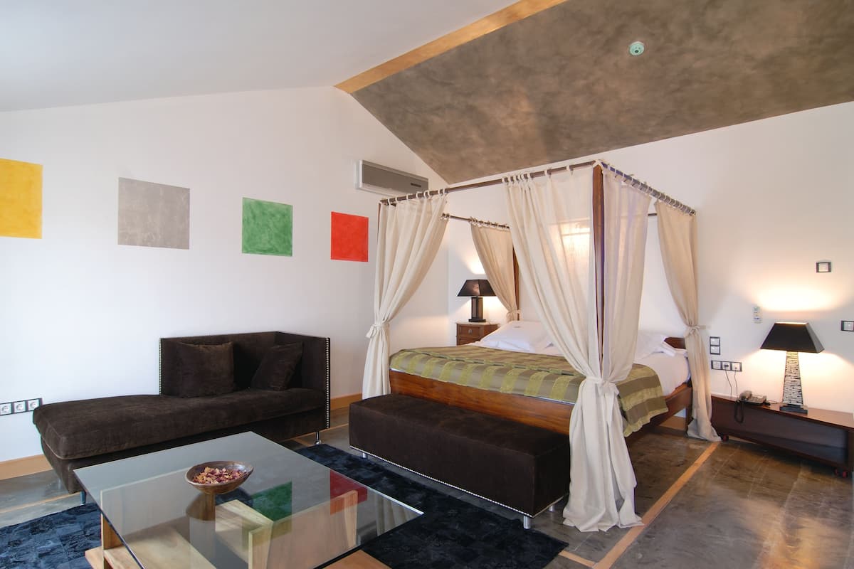 Um quarto com uma cama de dossel, um sofá, uma mesa de centro de vidro e uma mesa de cabeceira com uma luminária.