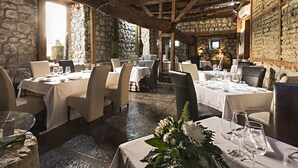 An indoor dining area with stone walls, wooden beams, and tables set for dining. - Rusticae Hotel Casa del Abad (Ampudia)