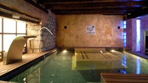 An indoor swimming pool with a stone wall, wooden deck, and a sign indicating a spa. - Rusticae Hotel Casa del Abad (Ampudia)