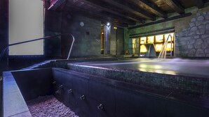 A spa area with a stone wall, a wooden ceiling, and a seating area with a bench and a small table. - Rusticae Hotel Casa del Abad (Ampudia)
