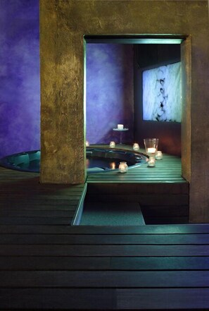 Un espacio de spa con suelo de madera, una pequeña piscina y velas.