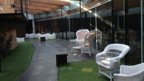 An outdoor seating area with wicker chairs and a small table, surrounded by glass walls and a stone wall. - Rusticae Hotel Casa del Abad (Ampudia)