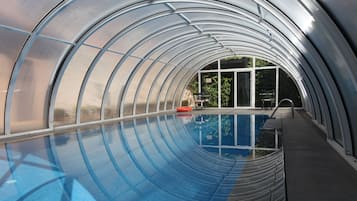 Una piscina techada, una piscina al aire libre, sombrillas