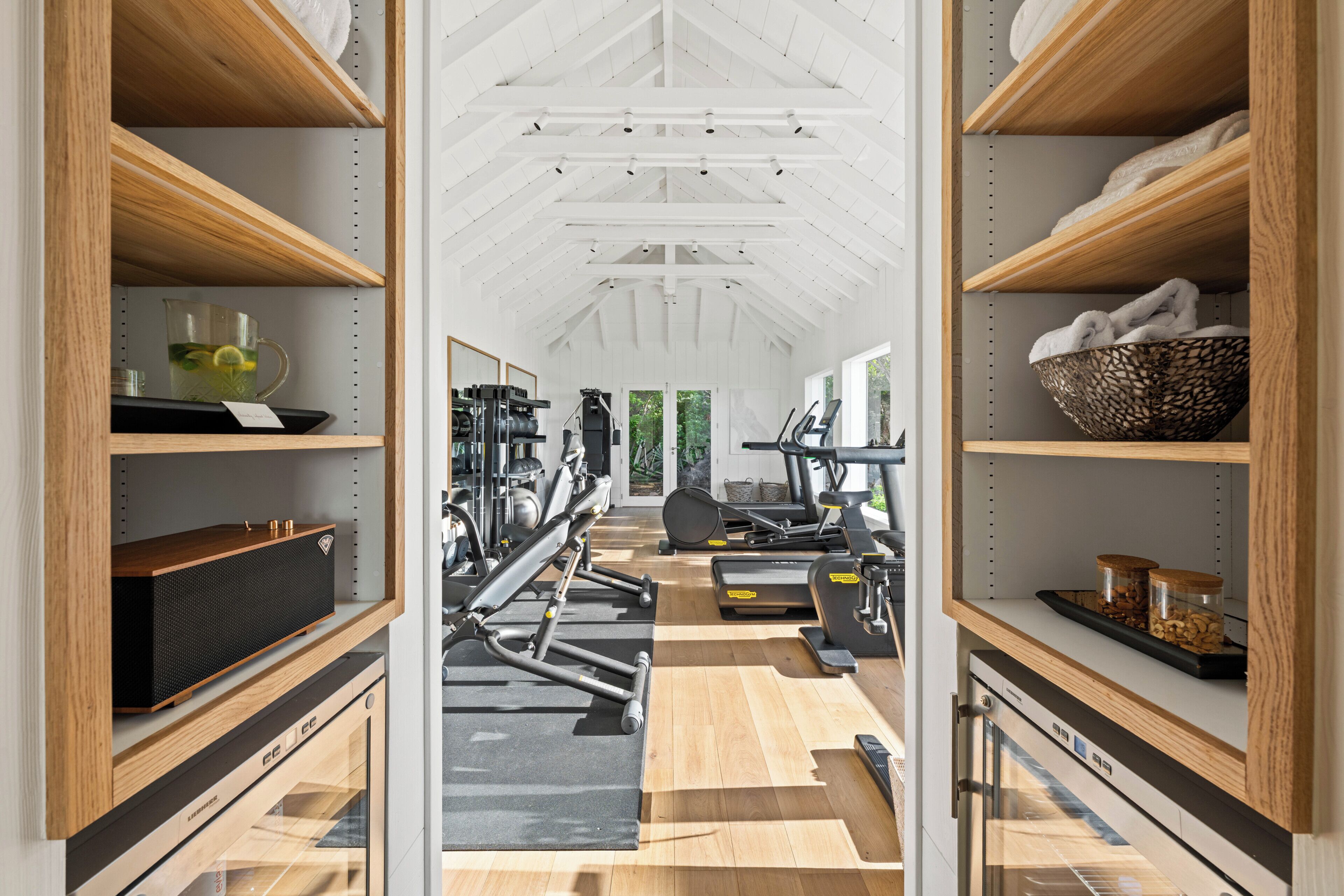 Un gimnasio con equipo de ejercicio, estanterías de madera y vistas al verdor.