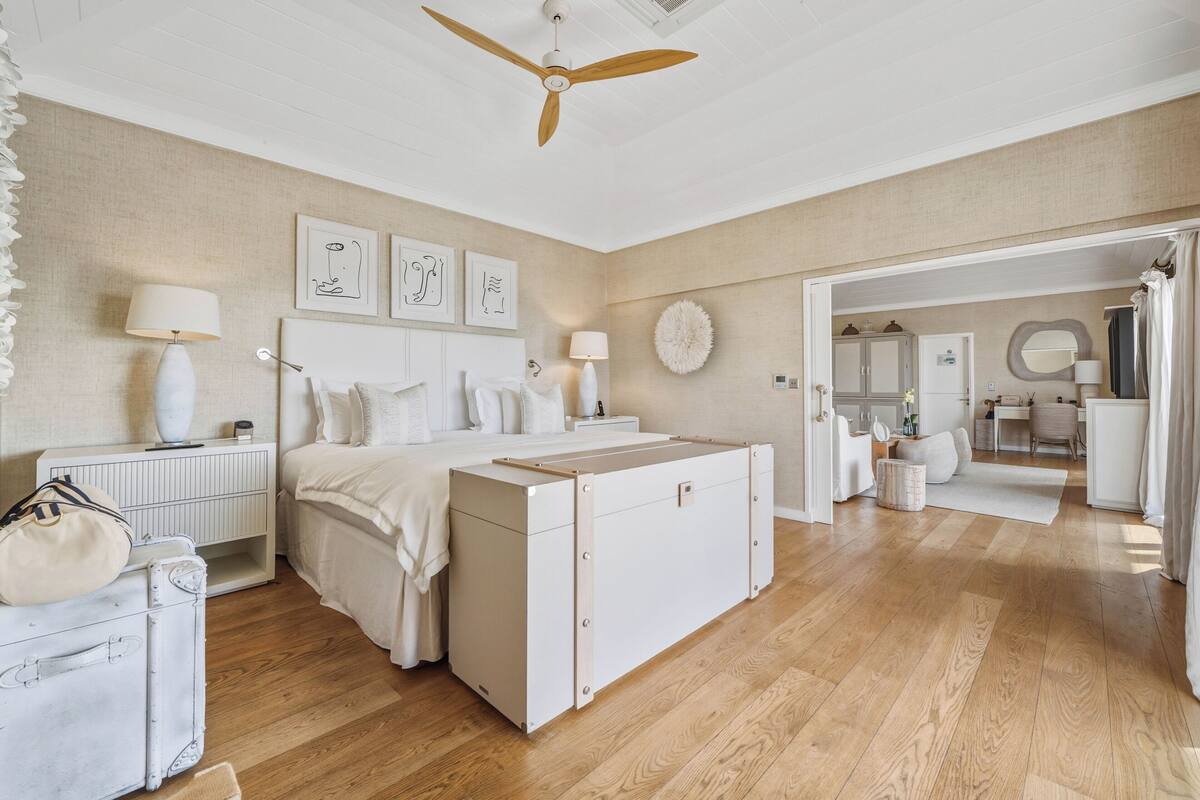 A bedroom with a bed, bedside tables, a dresser, a ceiling fan, and a view into the adjacent room.