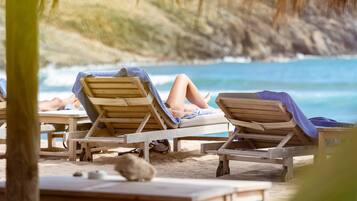 A beachside lounge area with wooden lounge chairs and a table, overlooking the ocean.
