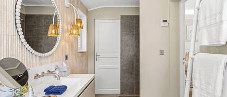 Un baño moderno con tocador, espejo, toallero y zona de ducha.