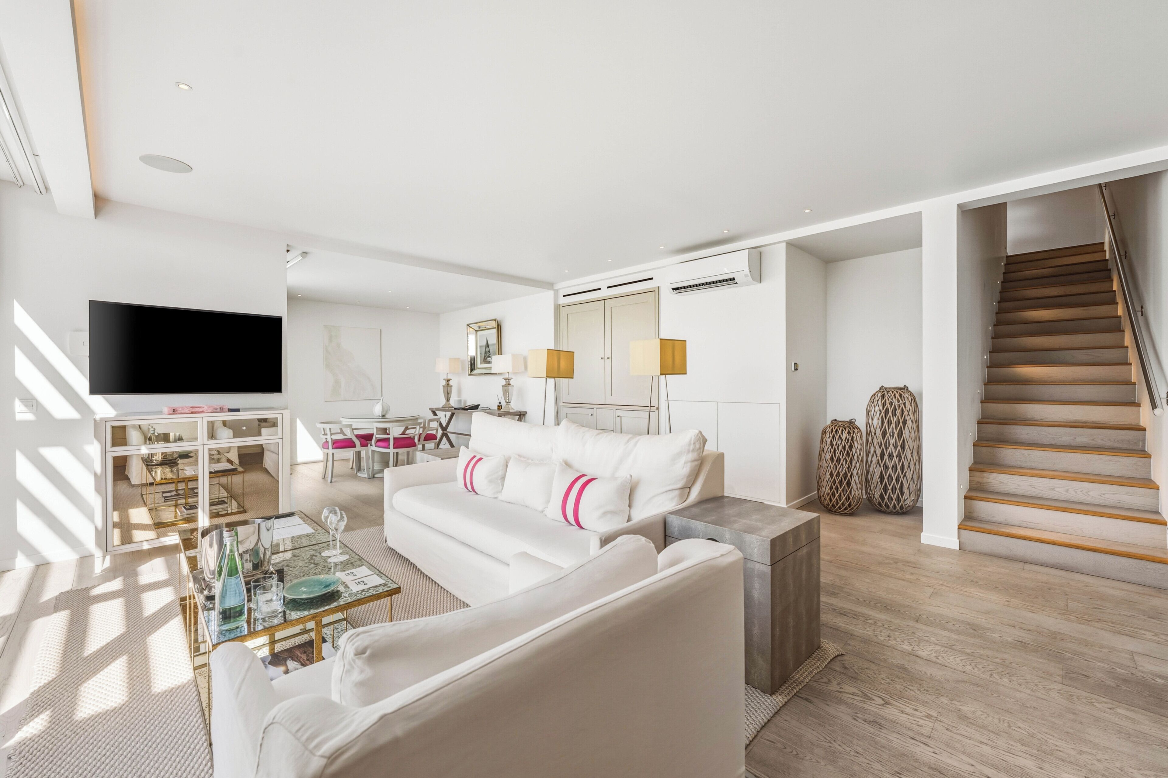 A modern living room with a flat-screen TV, white sofa, and a dining area with a table and chairs.
