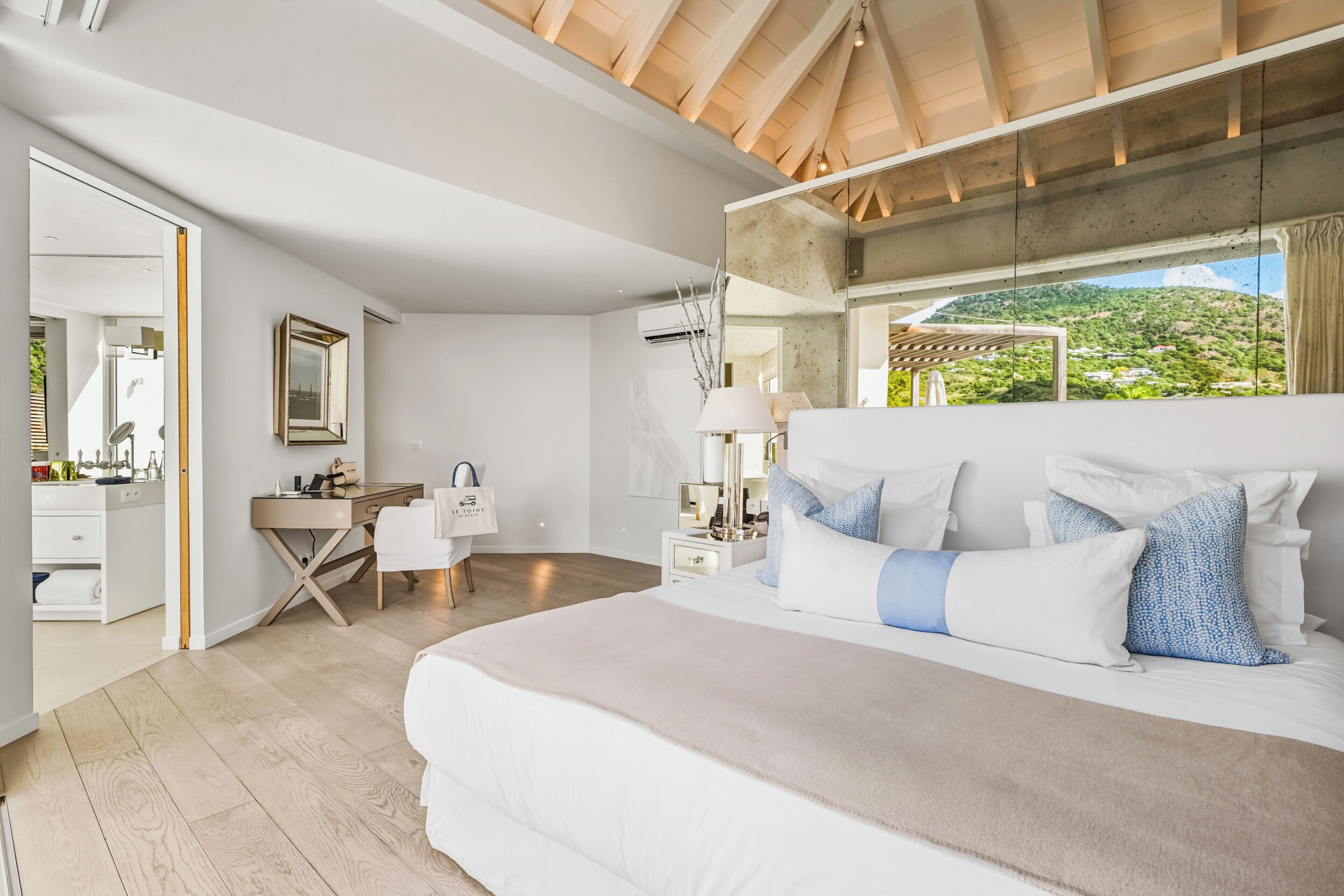 A modern bedroom with a large bed, a desk, and a view of a green landscape.