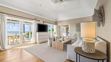 Een ruime woonkamer met houten vloer, een bank, salontafel, televisie en een balkon met uitzicht op zee.