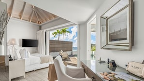 A modern hotel room with a bed, a desk, a chair, a TV, a large framed picture, and a view of the ocean. - Le Toiny Hôtel & Beach Club (St. Barthelemy)