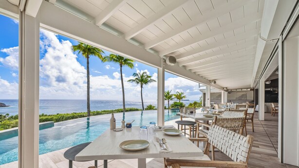 An infinity pool with a view of the ocean, outdoor dining area with tables and chairs, and palm trees. - Le Toiny Hôtel & Beach Club (St. Barthelemy)