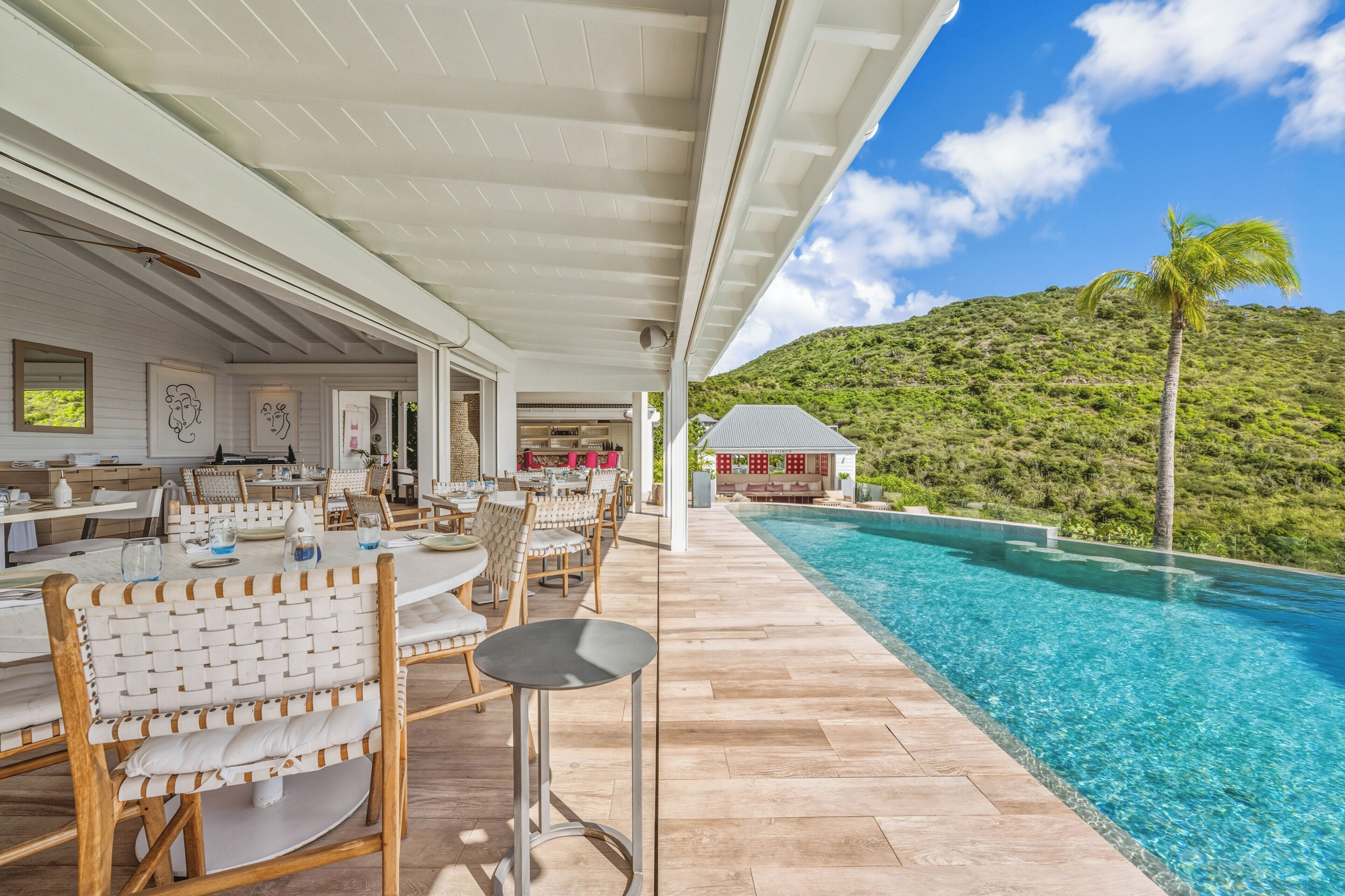 Un área junto a la piscina con mobiliario exterior, vista despejada de una montaña y un edificio al fondo.