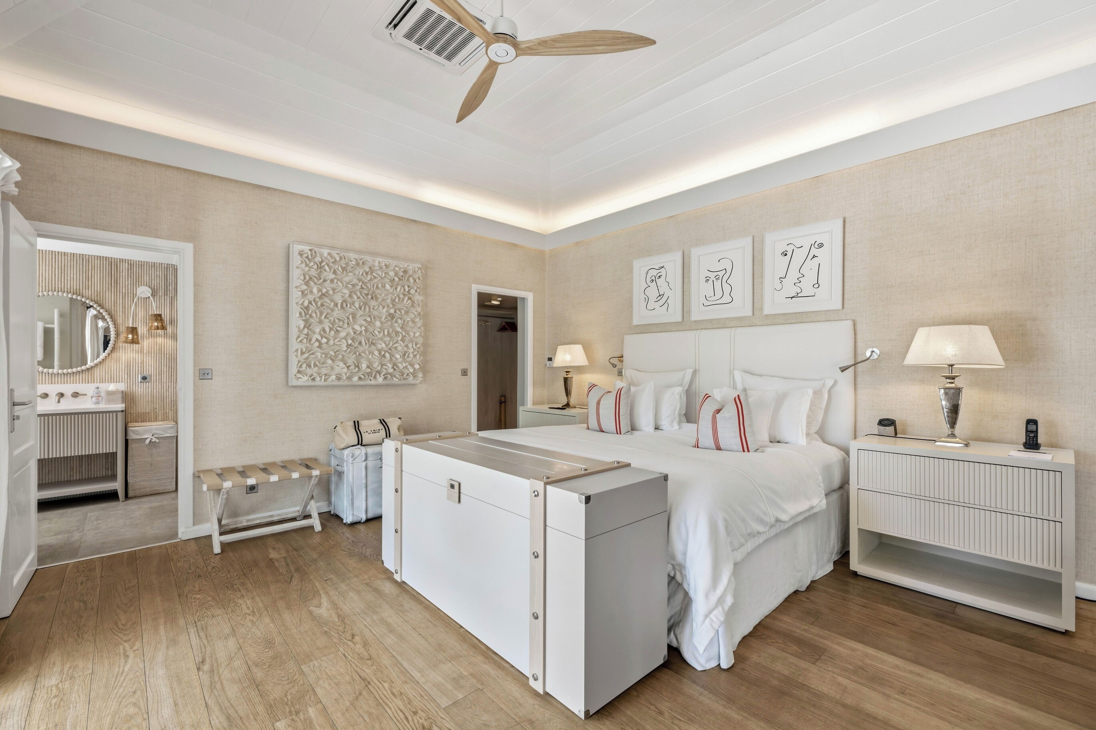 A hotel room with a bed, bedside tables, a bench, a mirror, and a ceiling fan.