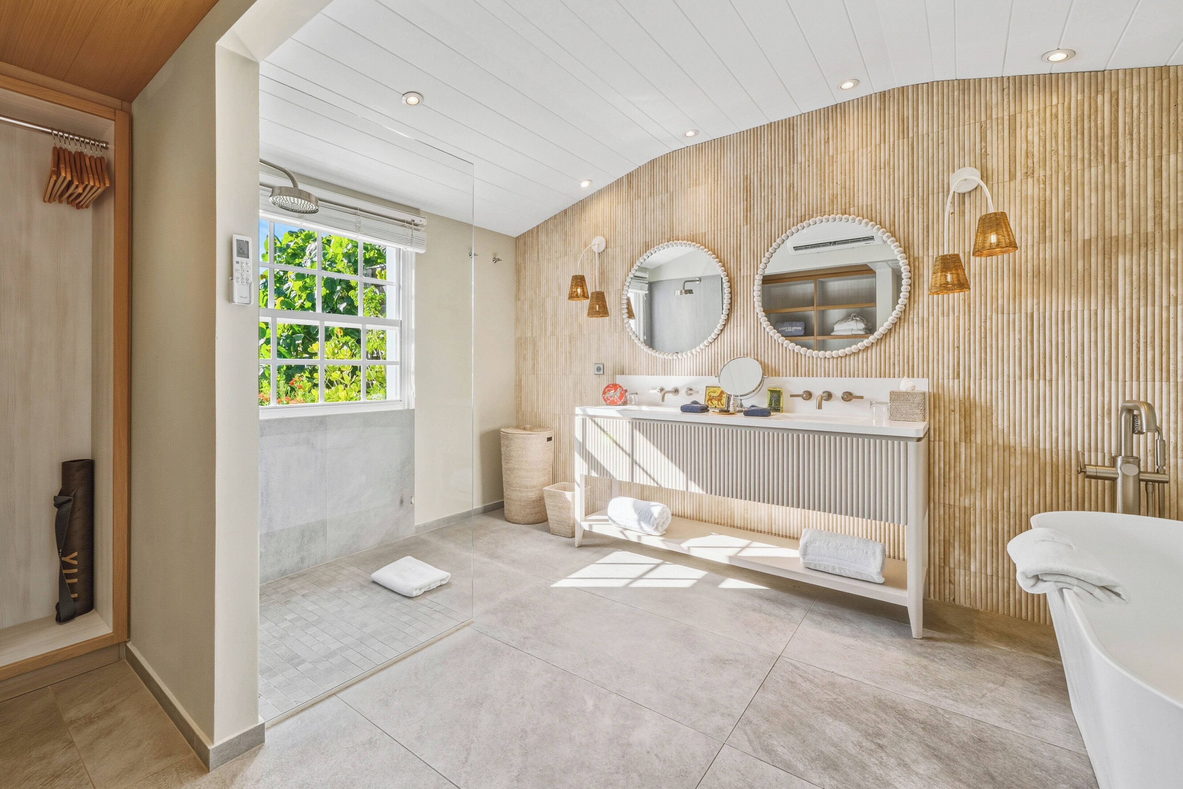 Un baño moderno con tocador, dos espejos, bañera y ventana con vistas a la vegetación.