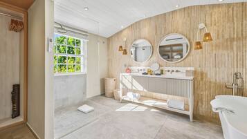 Un baño moderno con tocador, dos espejos, bañera y ventana con vistas a la vegetación.