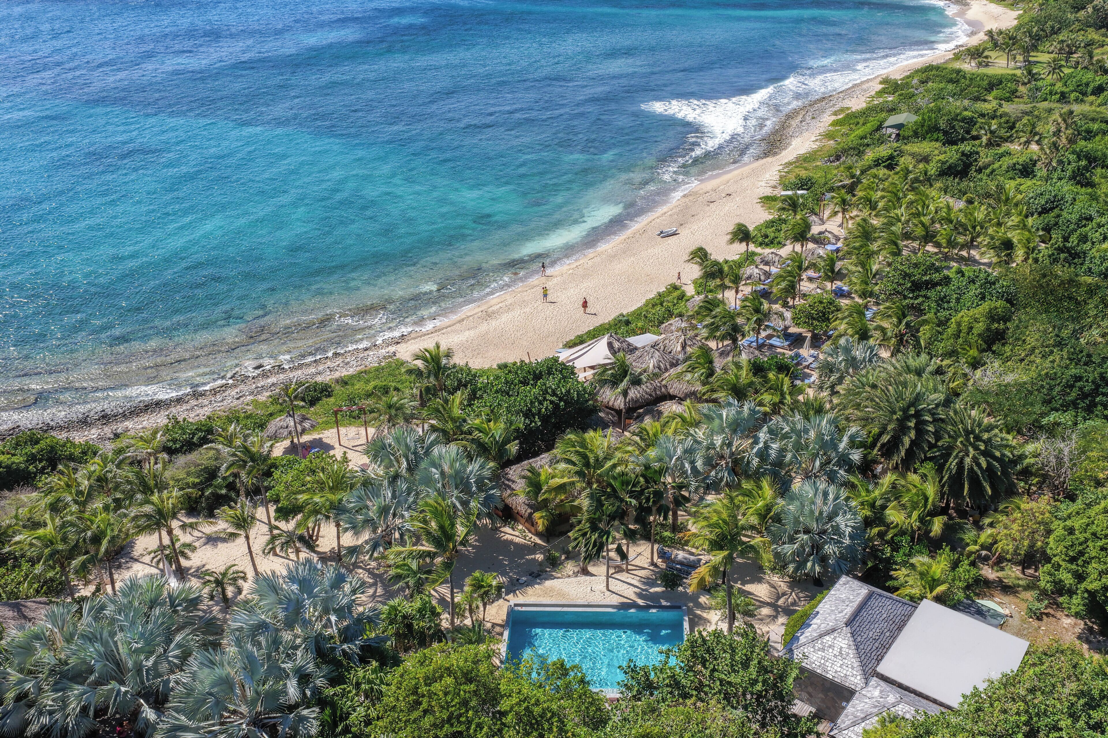 Vista aérea de un complejo turístico con piscina, palmeras y playa.