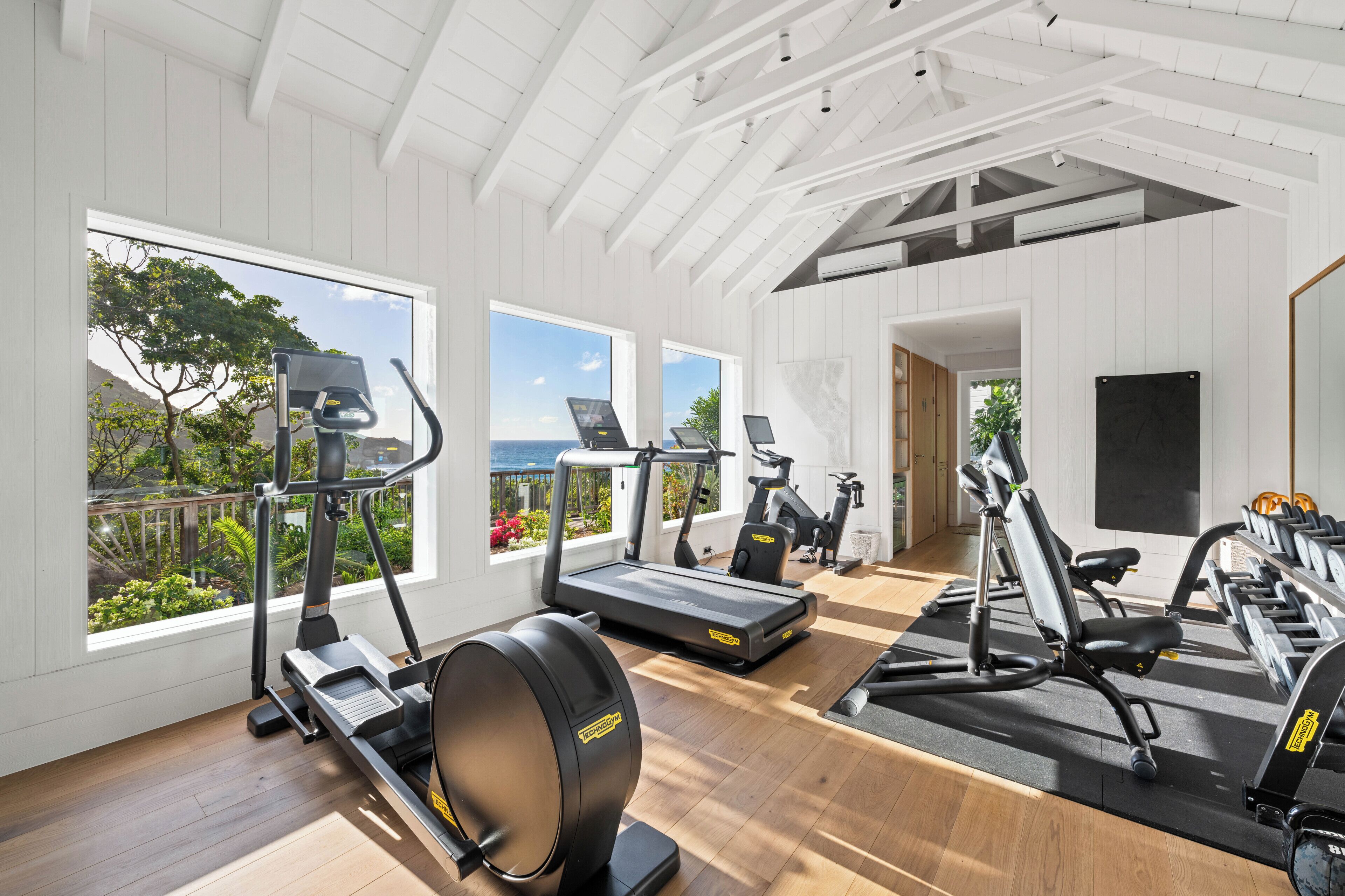 A gym with cardio machines, weight benches, and a view of the outdoors.