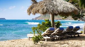 A beach with lounge chairs under a thatched umbrella, overlooking the ocean. - Le Toiny Hôtel & Beach Club (St. Barthelemy)