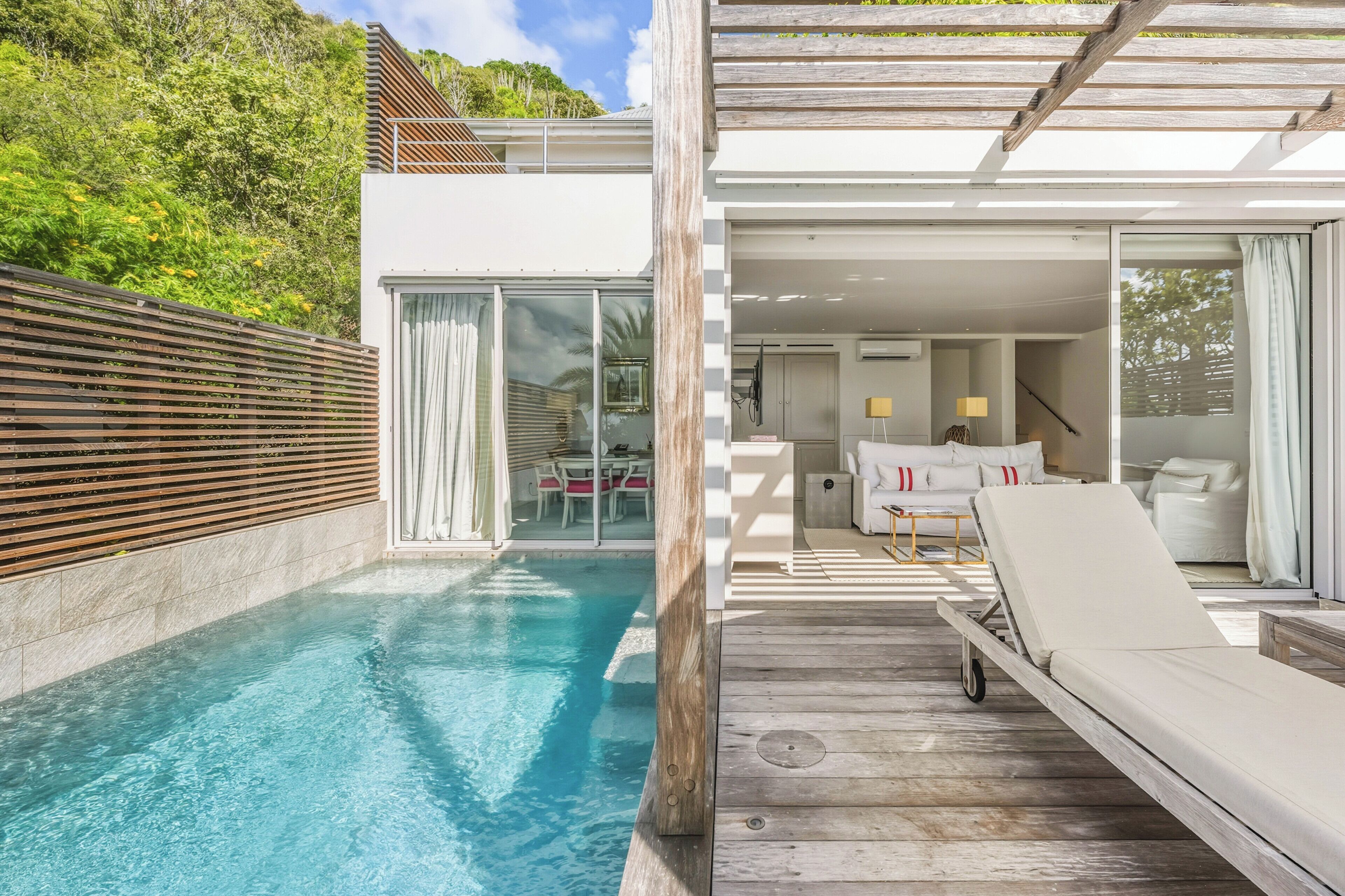 A modern poolside area with a wooden deck, a lounge chair, and a glass door leading to an interior space.