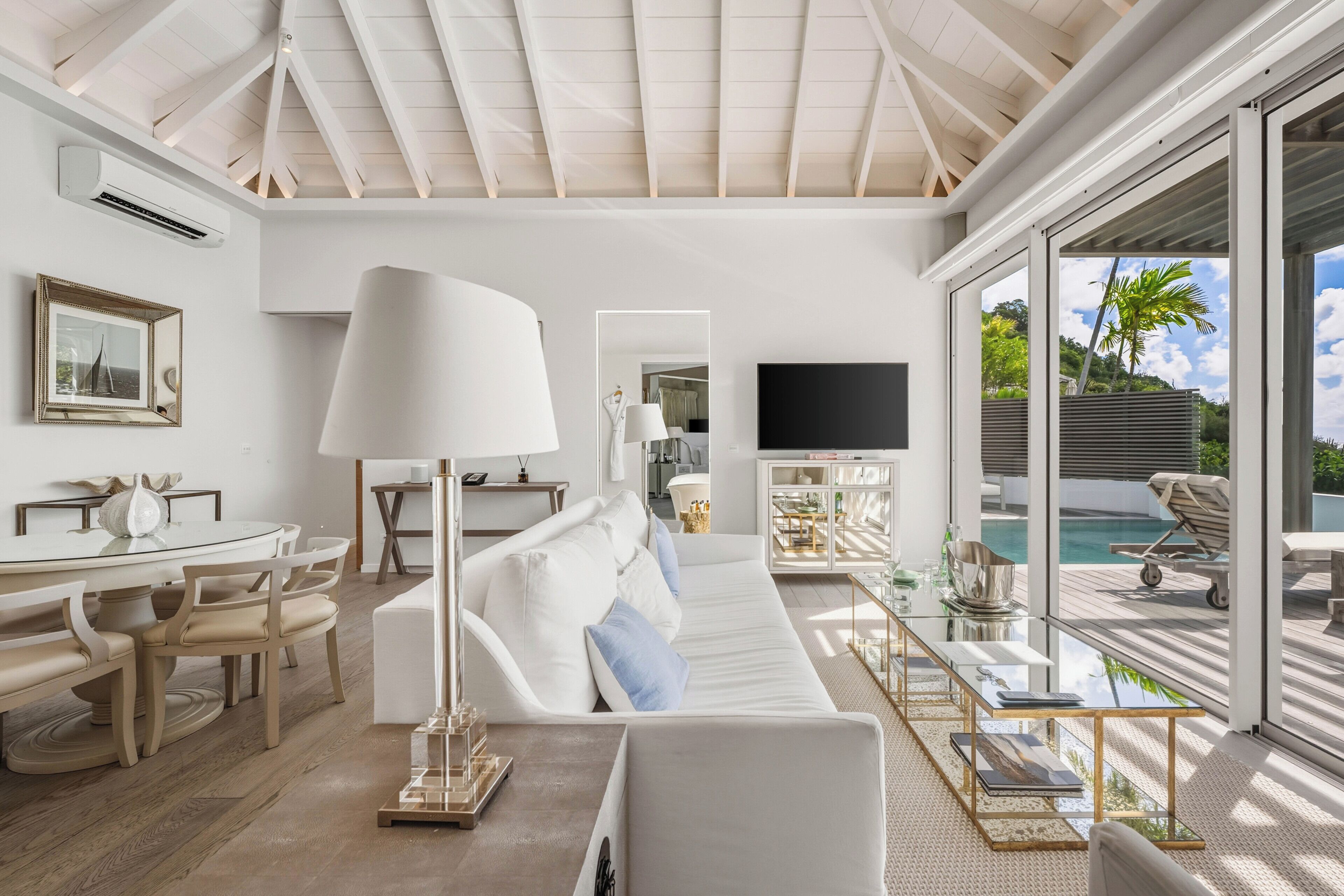 A modern living room with a white sofa, a dining table, and a TV.