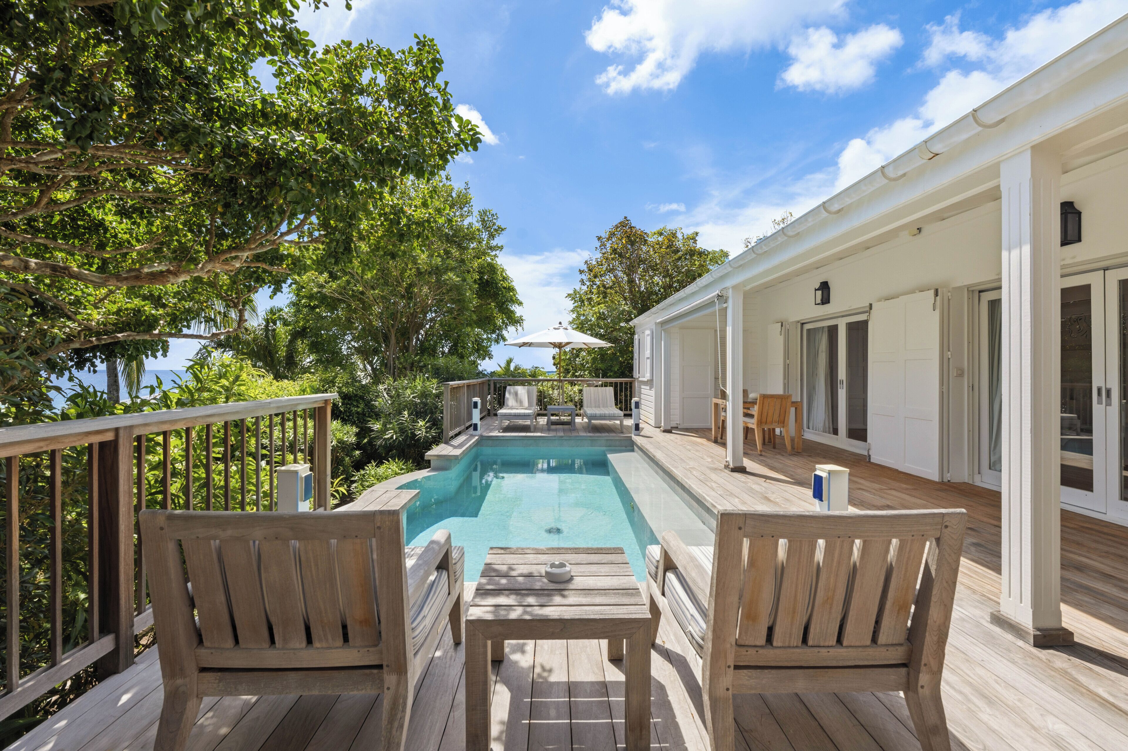 A wooden deck with a pool, outdoor furniture, and a covered area with doors.