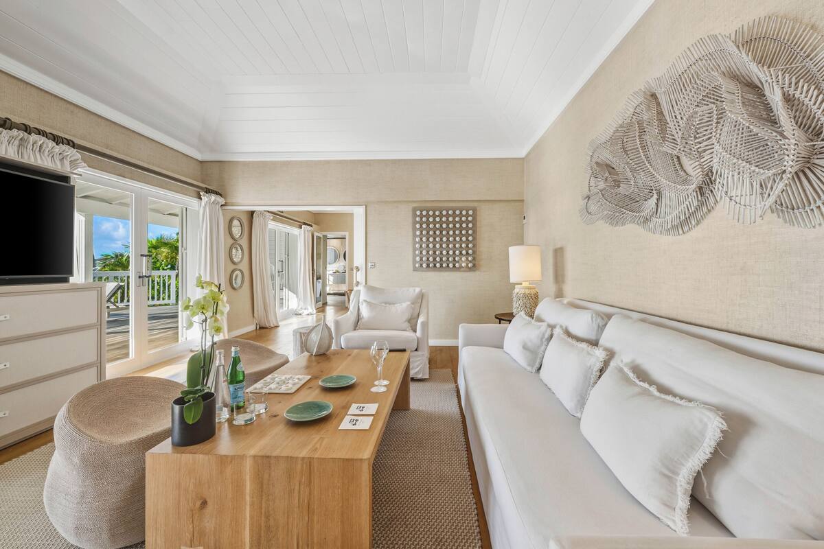 A modern living room with a wooden coffee table, white sofas, and a large wall art piece.