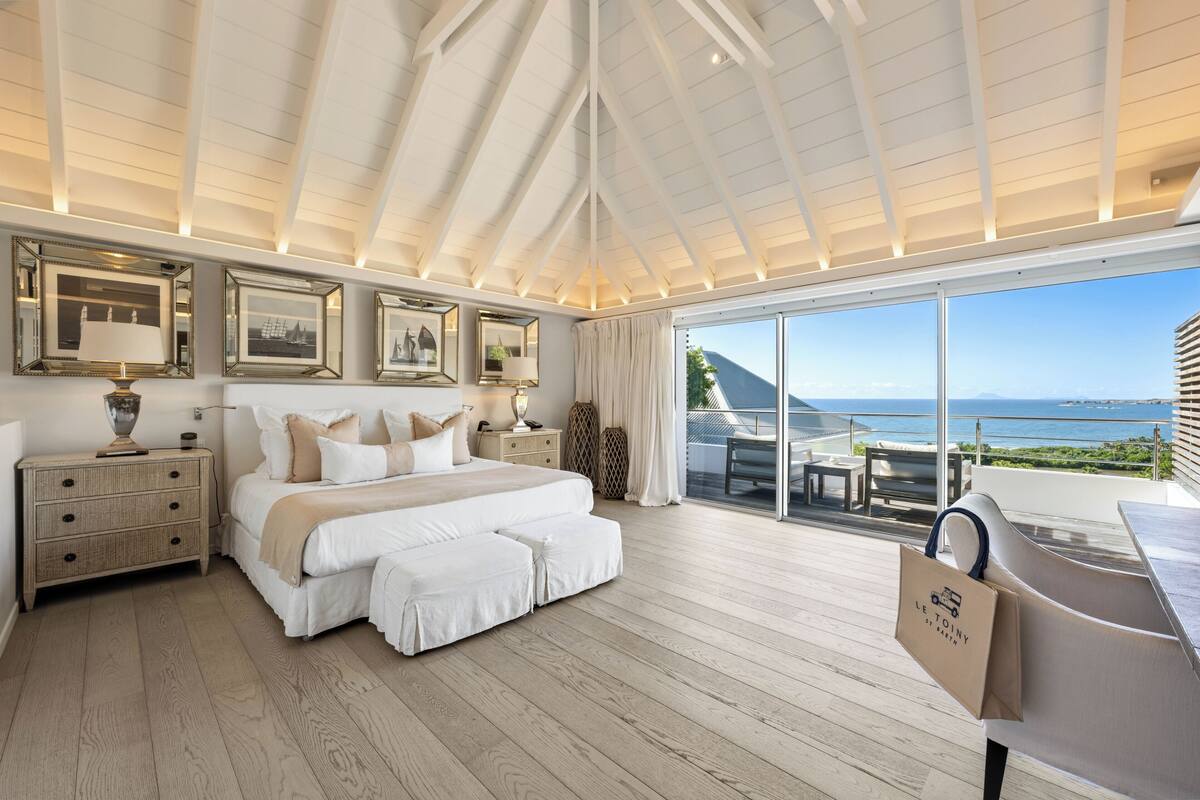 A spacious bedroom with a large bed, bedside tables, a nightstand, and a view of the ocean.