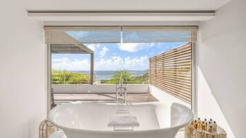 Ein modernes Badezimmer mit einer freistehenden Badewanne, einem weißen Waschbecken und Meerblick durch große Fenster.