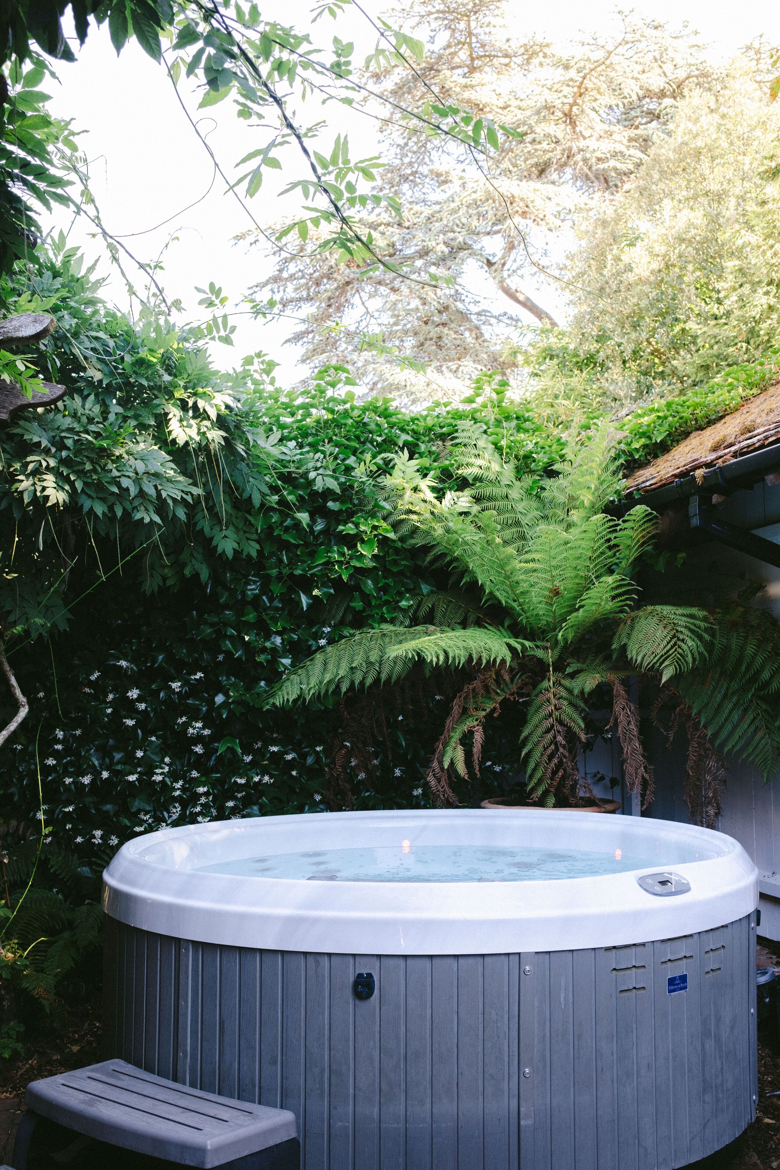 A hot tub surrounded by dense foliage and a wooden deck.