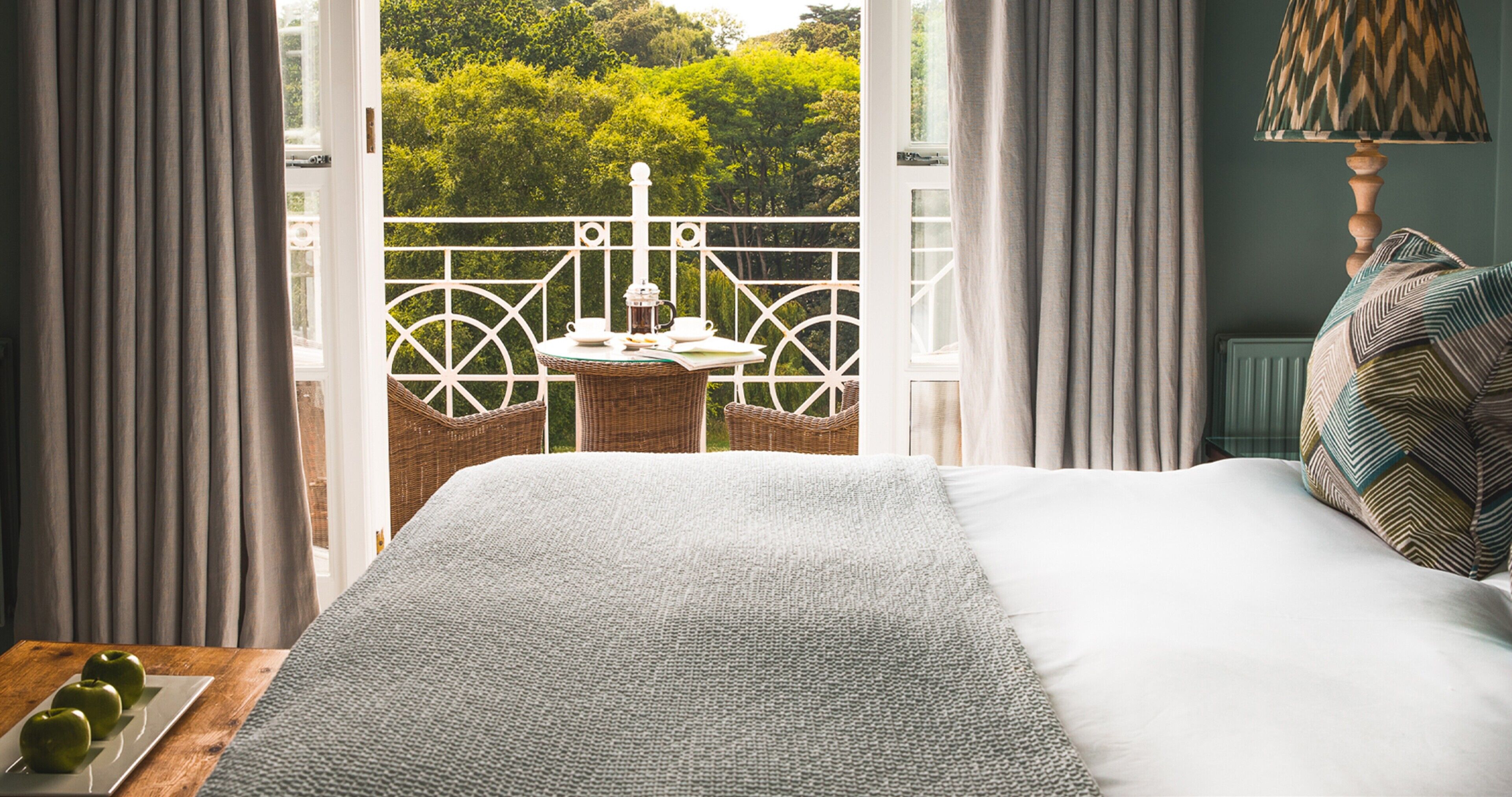 Quarto com uma cama grande, vista para uma varanda com mesa e cadeiras, e janela com cortinas.