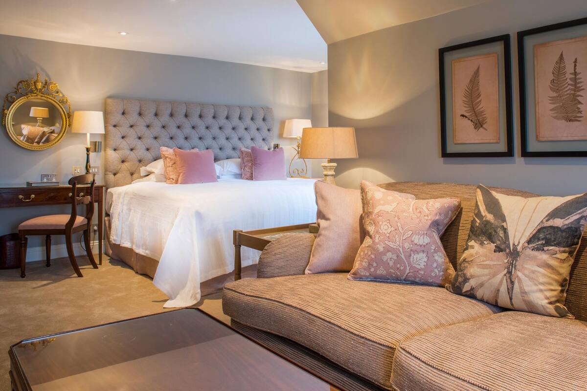 A hotel room with a large bed, a sofa, a desk, and framed botanical prints on the wall.