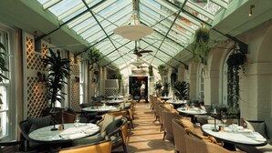 A spacious indoor dining area with high ceilings and a glass roof, featuring multiple tables and chairs arranged for dining. - Chewton Glen Hotel & Spa (New Milton)