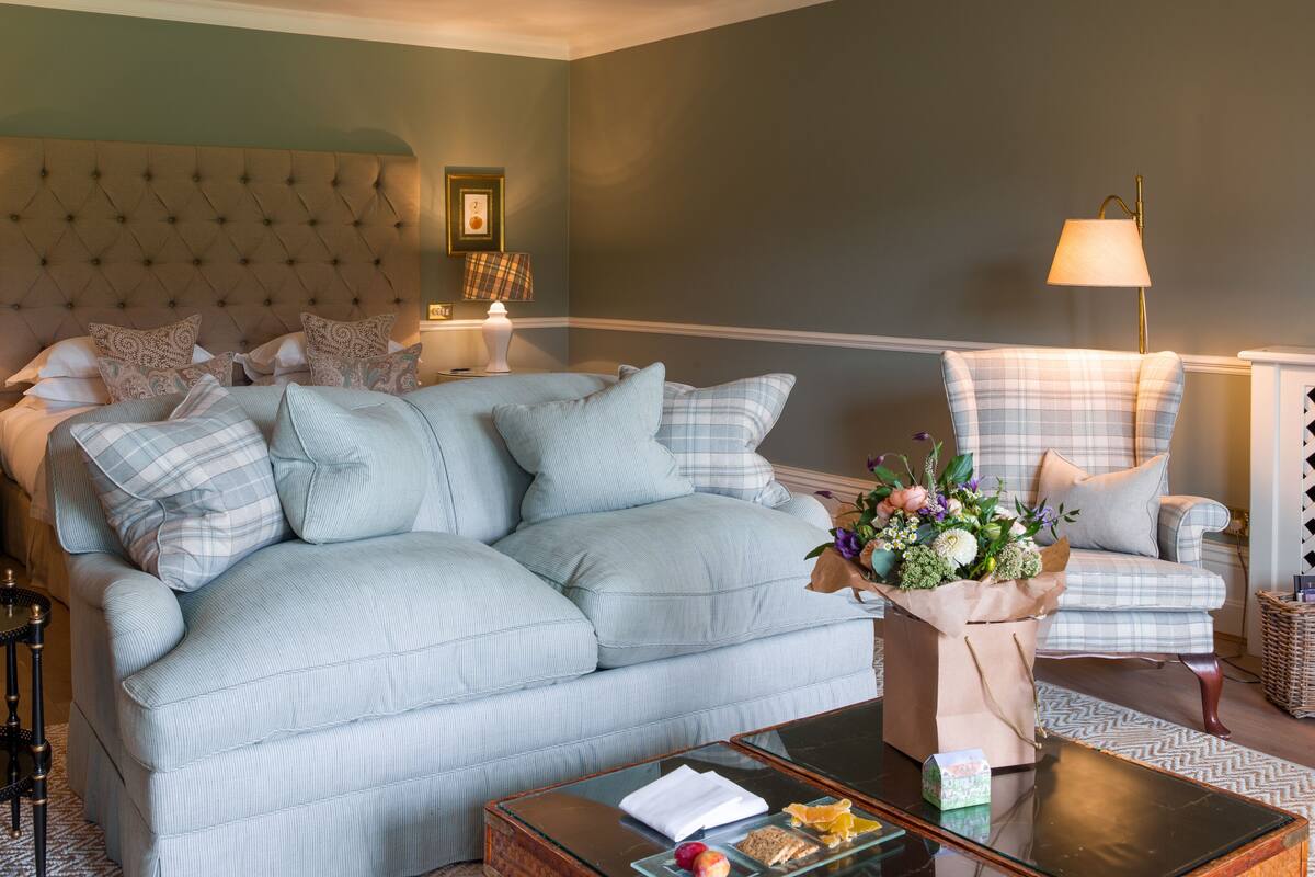 A well-appointed living room with a tufted headboard sofa, a plaid armchair, and a coffee table with a glass top.