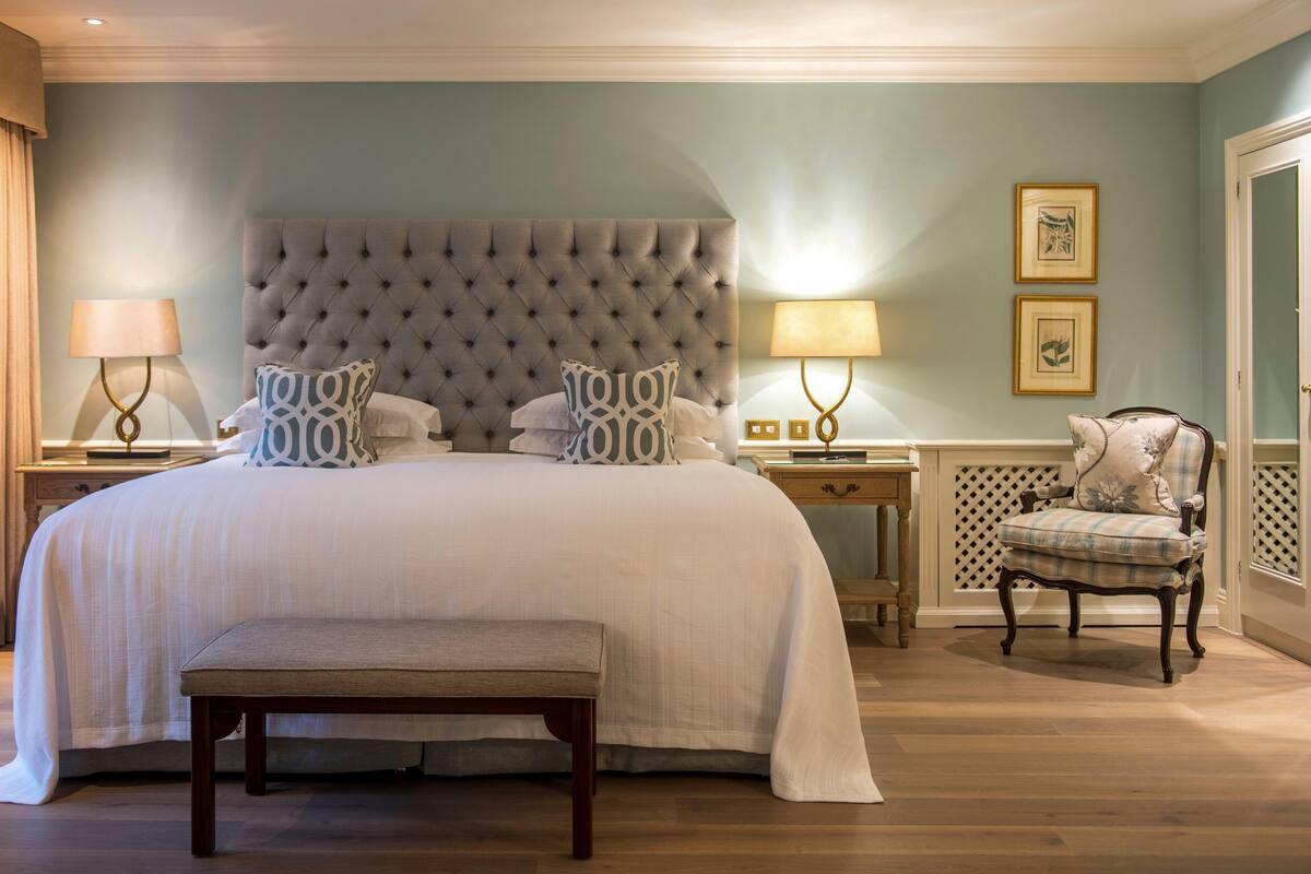 A spacious bedroom with a large bed, a bench, a chair, and two bedside tables with lamps.