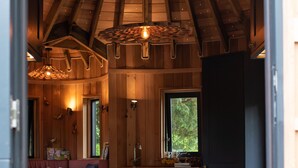 A cozy cabin interior with a wooden ceiling, a dining area, a kitchen, and a seating area with a sofa and cushions. - Chewton Glen Hotel & Spa (New Milton)