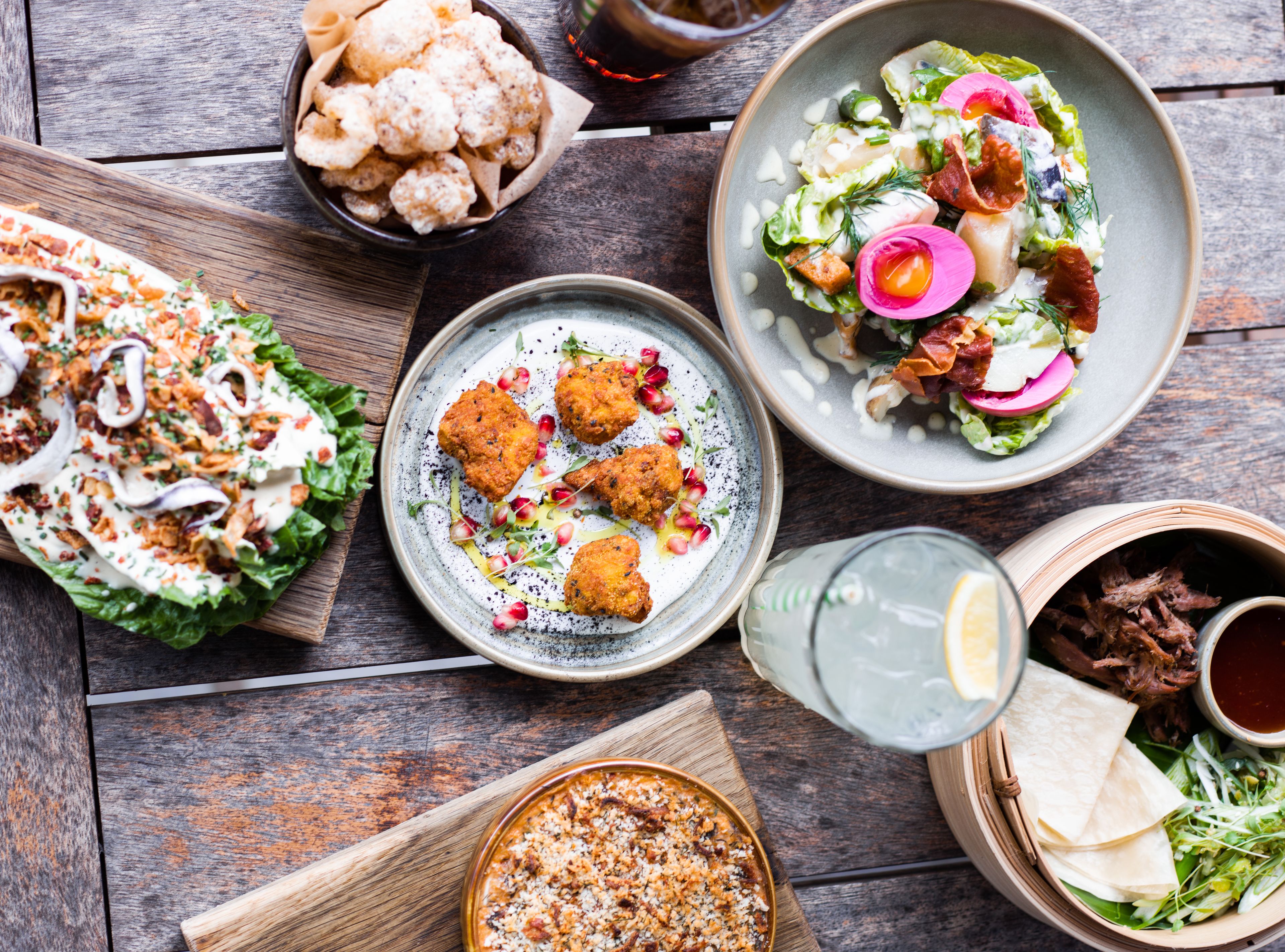 A variety of dishes on a wooden table, including a salad, fried items, and a bowl of popcorn.